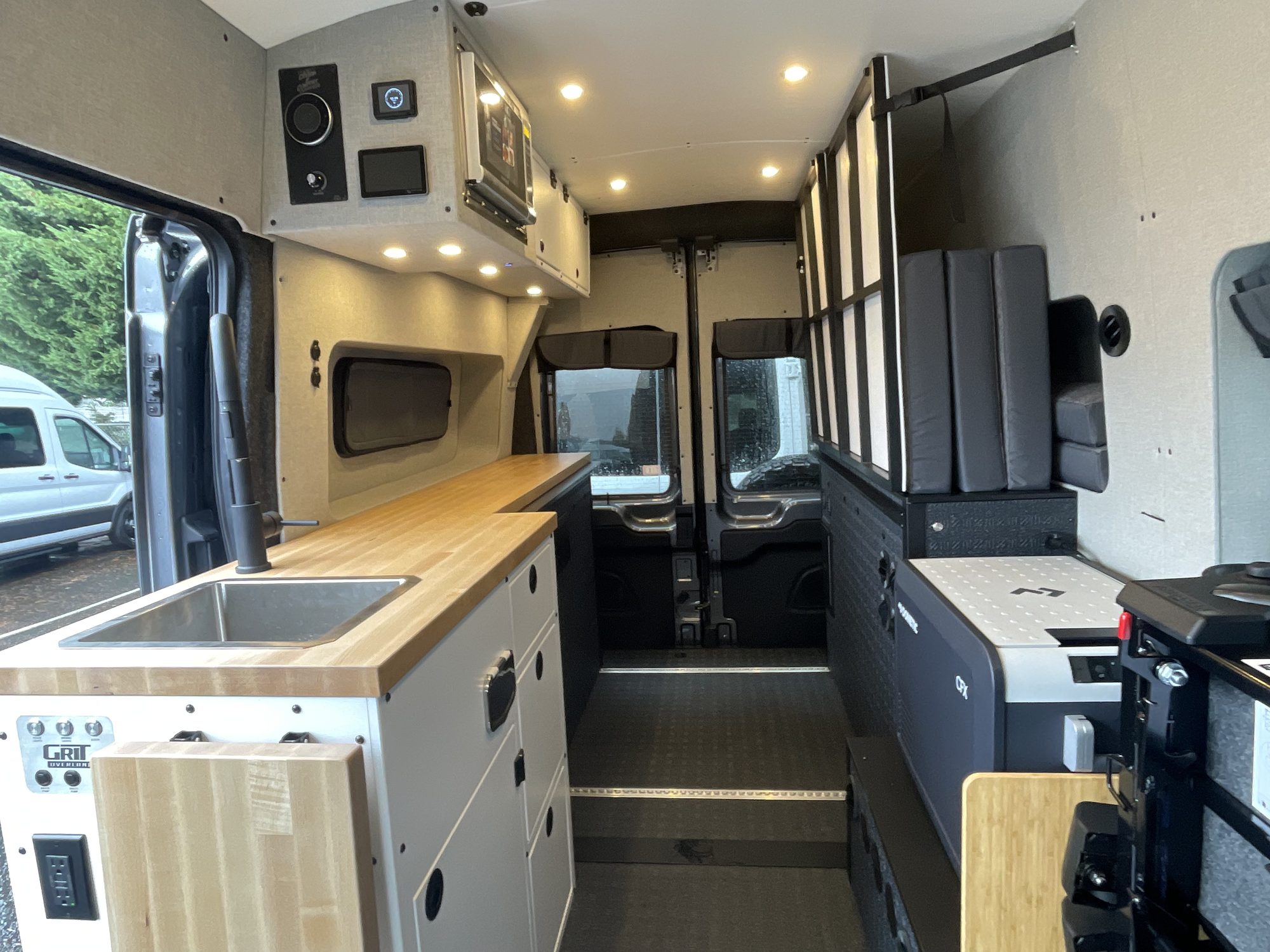 Interior looking forward: butcher-block counter with sink, aluminum cabinetry, overhead lights and the cab beyond