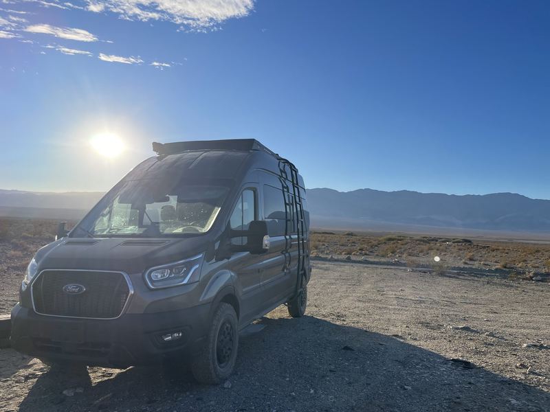 The van in the high desert with the sun flaring behind it and mountains in the distance