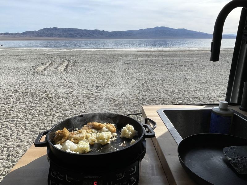 Cast iron skillet sizzling on the induction cooktop with a lake and mountains outside the door