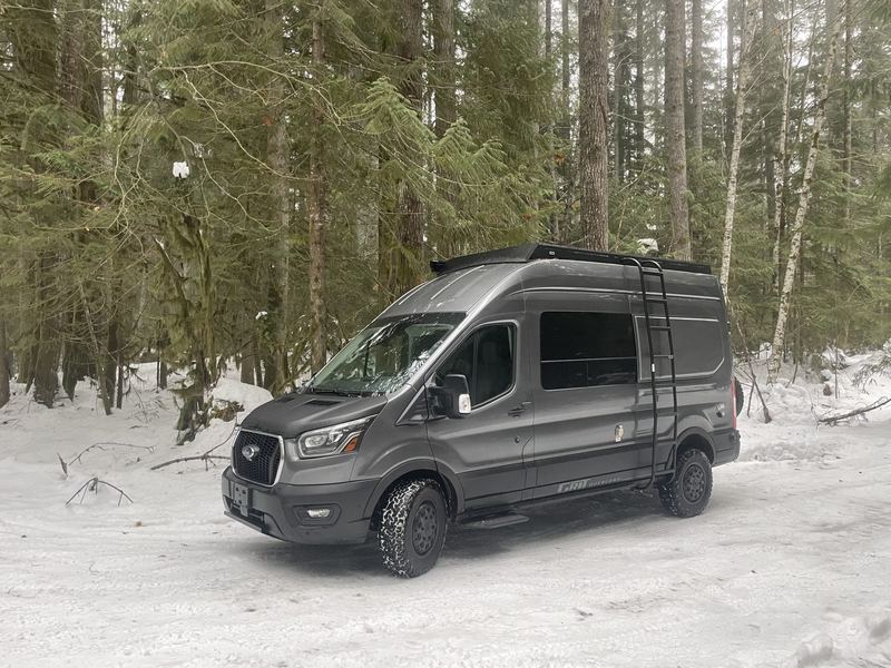 The van parked in fresh snow among evergreen trees