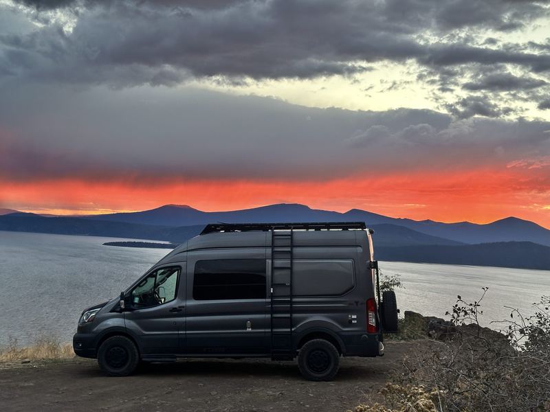 Van on a ridge above a lake at sunset